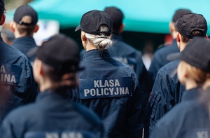 Uczmiowie klasy policyjnej stojący tyłem w czapeczkach na głowie. Na mundurach napis Klasa Policyjna.