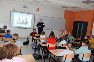 Policjant w sali lekcyjnej przedstawia dzieciom prezentację z omawianego zagadnienia