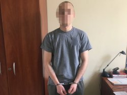 Jeden z zatrzymanych mężczyzn stojący przodem w kajdankach ubrany w szara koszulkę.