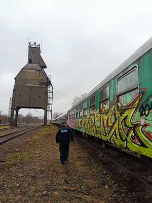 policjant idący wzdłuż torów kolejowych na których znajdują się pomalowane wagony