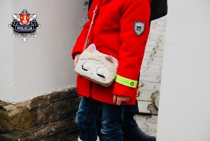 dziewczynka ubrana w czerwoną kurtke i torebke z kotkiem ma założona na ręce odblaskową opaskę