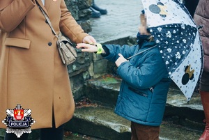 mama zakłada córce trzymającej parasol opaskę odblaskową