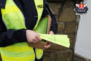policjantka trzymająca opaski odblaskowe do rozdania na których widnieje napis makow podhalański i logo makowa