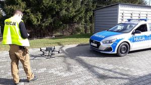 Obok policjanta i radiowozu stoi dron