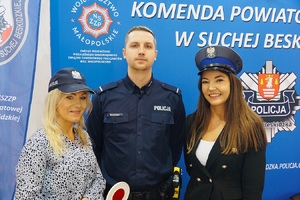 Pozujące do zdjęcia dwie panie w czapkach policyjnych  z policjantem