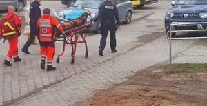 Zdjęcie z interwencji w Brzeszczach ratownicy medyczni i policjanci pchają nosze po uliczce w tle zaparkowane samochody