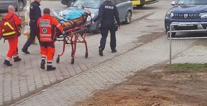 Zdjęcie z interwencji w Brzeszczach ratownicy medyczni i policjanci pchają nosze po uliczce w tle zaparkowane samochody