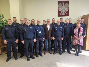 Na zdjęciu widać umundurowanych policjantów oraz policjantki oraz kobietę i mężczyznę w stroju cywilnym. Na  ścianie Godło Polski.