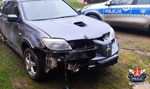rozbity w przedniej części czarny samochód za którym stoi oznakowany policyjny radiowóz