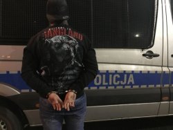 Zatrzymany mężczyzna z kajdankami na rękach trzymanych z tyłu. w tle radiowóz OPP w Krakowie, Mercedes Sprinter