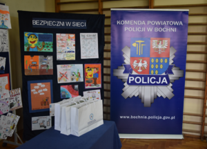 Baner Komendy Powiatowej Policji w Bochni, tablicami z rysunkami bioracymi udział w konkursie oraz białe torby z nagrodami