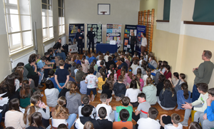 Umundurowani policjanci, dyrekcja, pedagodzy oraz ucznioiwie szkoły. Za policjantami stoją tablice z rysunkami biorącymi udział w konkursie oraz baner komendy