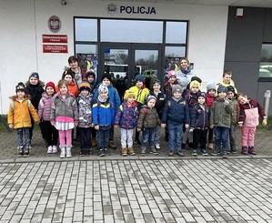 Na zdjęciu na tle budynku Komendy Powiatowej Policji w Wadowicach stoi grupa dzieci, przodem, Po prawej i po lewej stronie kobieta w stroju cywilnym.