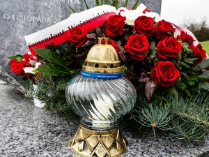 Znicz  a za nim wieniec z czerwonych róż z biało czerwoną wstęgą