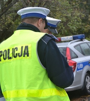 policjanci ruchu drogowego w kamizelkach odlaskowych białych czapkach a w tle radiowóz oznakowany