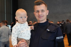 Policjant w mundurze trzymający na prawej ręce dziecko.