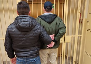 nieumundurowany policjant oczekujący z osobą zatrzymaną przed wejściem do policyjnego aresztu
