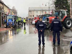 stojący tyłem policjanci w tle ciagnik rolniczy i chodzący uczestnicy zgromadzenia