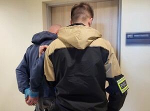 nieumundurowany policjant prowadzący zatrzymanego z kajdankami na ręce trzymane z tyłu. (2)