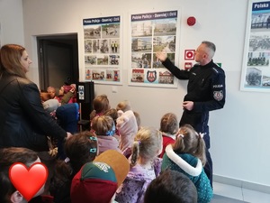 Policjant prezentujące dzieciom tablice z informacjami na temat pracy policjantów w dawnych latach i jak wygląda słuzba obecnie