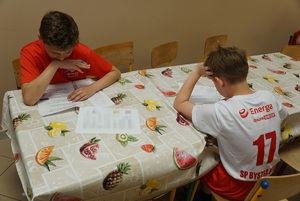 1. siedzący chłopcy przy stole i rozwiązujący testy w turnieju