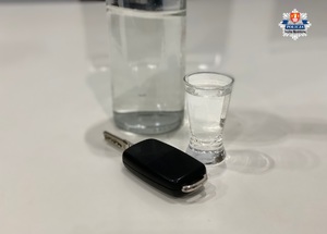 napełniony kieliszek, którego tłem jest pełna butelka a obok kluczyki od samochodu na białym stole