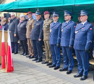 Na zdjęciu przed namiotem widać trzech umundurowanych policjantów w strojach galowych, przedstawicieli wojska, służby więziennej i osoby cywilne.