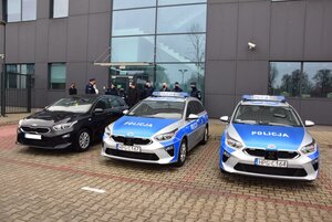 Trzy radiowozy stojące na parkingu przed KPP w Krakowie, w tle Komendant Powiatowy Policji w Krakowie ze Starostą Krakowskim oraz zaproszonymi gośćmi.