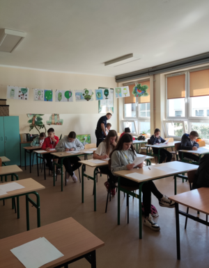 Umundurowany policjant oraz uczniowie piszący test wiedzy