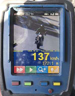Zdjęcie wykonane fotoradarem ręczny, na którym uwidocznione jest czarny motocyklista, poniżej prędkość, z jaką się poruszał motocykl 137  kilometrów na godzinę