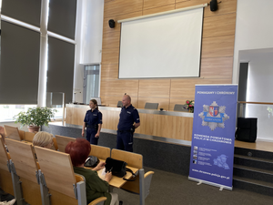umundurowani policjanci w budynku edukują seniorów na temat bezpieczeństwa w tle rolap Komendy Powiatowej Policji w Chrzanowie