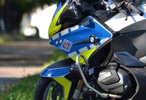 Widok zaparkowanego motocykla policyjnego przy drodze biegnącej przez las