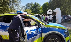 Piknik charytatywny na Jacusia 12.05 (2) policjant prezentuje radiowóz chłopiec siedzi za kierownicą w tle maskotki