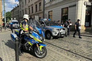 policjanci zabezpieczający Marsz Równości i uczestnicy marszu, wdoczny policjant na motocyklu i radiowóż z nagłosnieniem