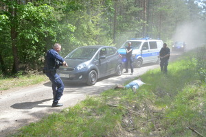 dwaj umundurowani policjanci w ręku z bronią ubezpieczają policjanta, który będzie zakładał kajdanki zatrzymanemu napastnikowi