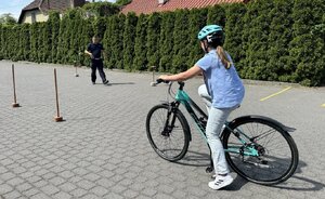 policjant nadzoruje część teoretyczną podczas egzaminu na kartę rowerową. uczennica przygotowuje się do pokonania toru przeszkód