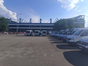 oznakowane radiowozy zaparkowane przed stadionem Wisły Kraków. Obok widać kibiców zmierzających na mecz