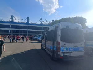 policyjne radiowozy stojące przed stadionem obok którcyh przechodzą kibice wychodzący ze stadionu