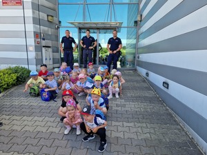 Trzej dzielicowi z grupa przedszkolaków przed budynkiem komendy