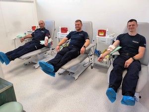 Trzech umundurowanych policjantów siedzących na szpitalnych łóżkach, którzy oddają krew