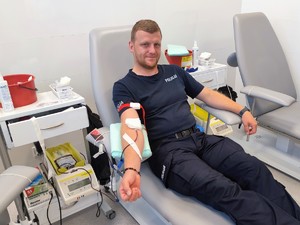 Umundurowany funkcjonariusz Policji siedzący na łóżku szpitalnym, który oddaje krew
