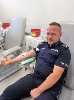 Umundurowany policjant siedzący na łóżku szpitalnym oddający krew