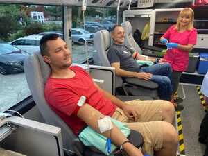 dwóch mężczyzn siedzących na fotelach oddających krew, przy jednym z nich stoi pielęgniarka