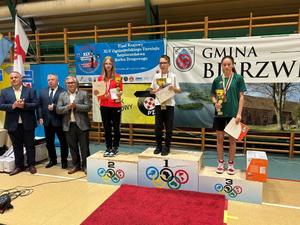 Na podium stoją trzy osoby, obok organizatorzy turnieju