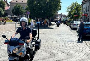 Policjanci ruchu drogowego na motocyklach pzabezpieczaja przemarsz. W tle ludzie, olkuski rynek i zabudowania. Pogoda letnia słoneczna.  oraz