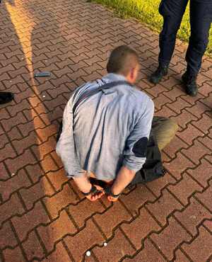 Zatrzymany siedzący na kostece brukowej z rękami skutymi do tyłu