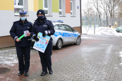 nr 3 – na zewnątrz przed budynkiem szkoły stoją dwie policjantki. Policjantka ruchu drogowego trzyma w ręku odblaski oraz ulotki, policjantka prewencji trzyma w ręku plakat. W tle zaparkowany radiowóz policyjny.