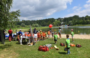 Dzieci biorące udział w prelekcji na tle zalewu wodnego Na zdjęciu widoczny również fragment policyjnego radiowozu