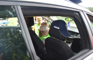 Dzieci w policyjnym radiowozie. Na siedzeniu czapka z napisem Policja