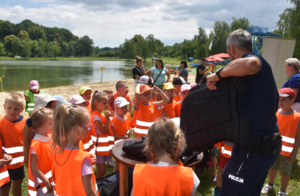 Profilaktyka nad zalewem wodnym. Dzieci w kamizelkach odblaskowych, wychowawcy oraz umundurowany policjant trzymający w rękach policyjną kamiezelkę